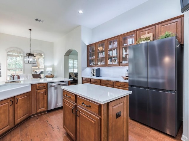 kitchen with appliances with stainless steel finishes, arched walkways, brown cabinetry, decorative light fixtures, and wood finished floors