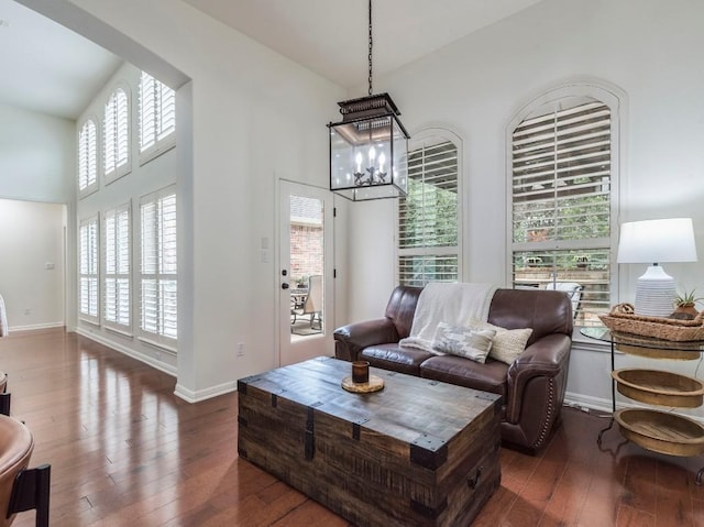 living area with baseboards, high vaulted ceiling, a notable chandelier, and hardwood / wood-style floors