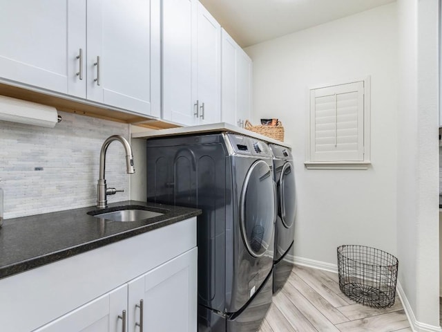 laundry area featuring washing machine and clothes dryer, cabinet space, a sink, baseboards, and light wood-style floors