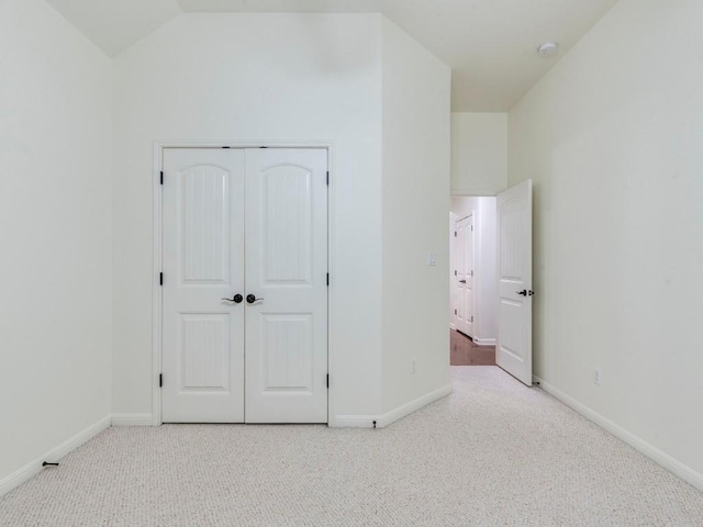 unfurnished bedroom with a closet, carpet floors, baseboards, and vaulted ceiling