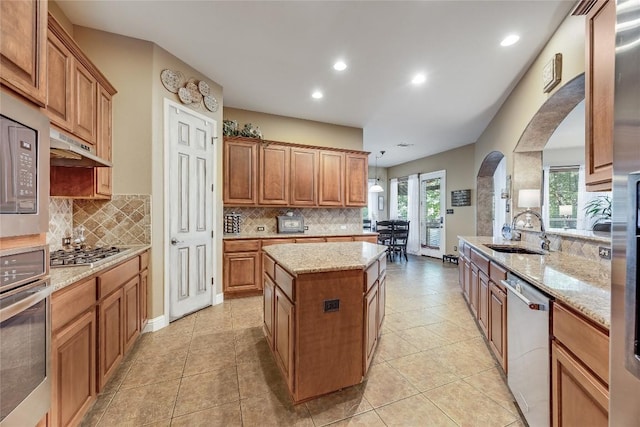 kitchen featuring arched walkways, under cabinet range hood, tasteful backsplash, a sink, and stainless steel appliances