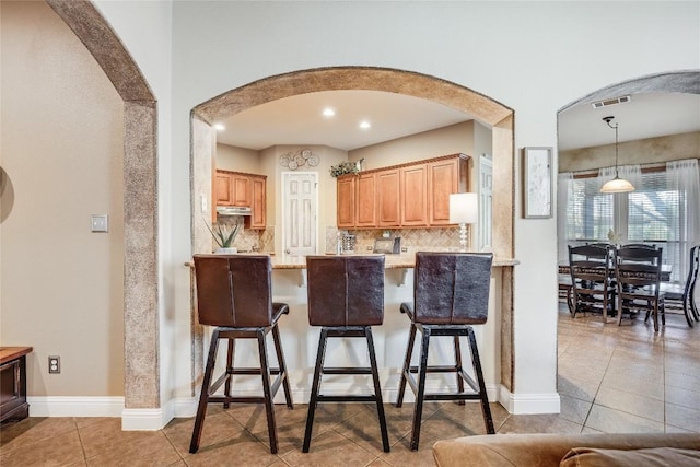 kitchen with visible vents, a kitchen bar, under cabinet range hood, arched walkways, and light tile patterned floors