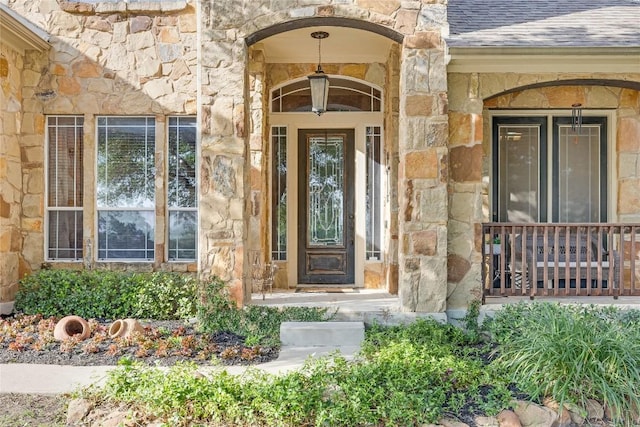 view of exterior entry with roof with shingles and stone siding