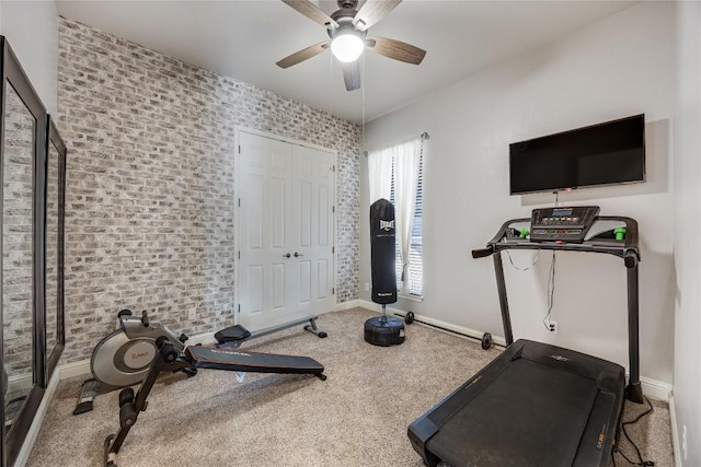 exercise room featuring baseboards, carpet flooring, brick wall, and ceiling fan