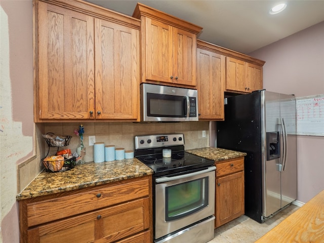kitchen with brown cabinets, stainless steel appliances, decorative backsplash, and dark stone counters