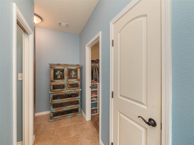 corridor with visible vents, baseboards, and light tile patterned floors