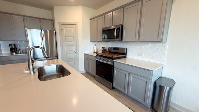kitchen featuring gray cabinetry, appliances with stainless steel finishes, tasteful backsplash, and a sink