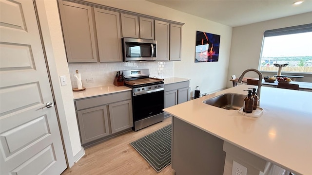 kitchen with decorative backsplash, appliances with stainless steel finishes, gray cabinetry, a sink, and light wood finished floors
