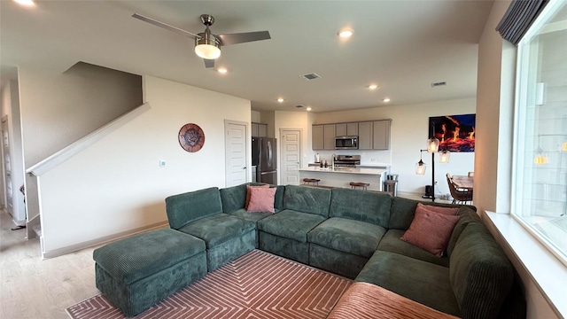 living room with a ceiling fan, visible vents, light wood-type flooring, baseboards, and recessed lighting