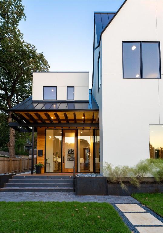 back of house featuring metal roof, stucco siding, fence, and a standing seam roof