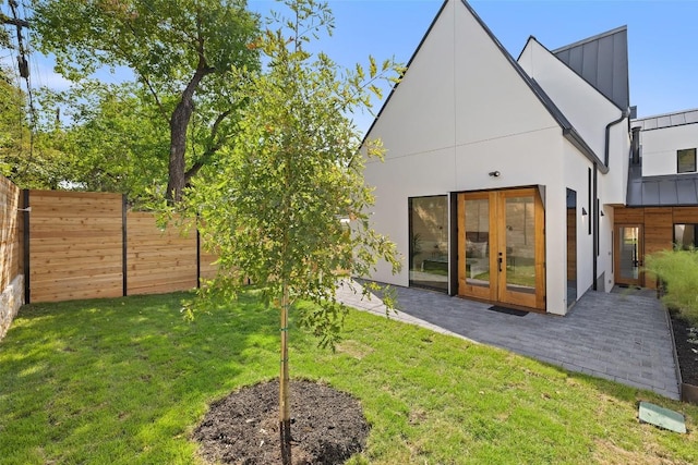 rear view of property featuring fence, stucco siding, french doors, a patio area, and a yard