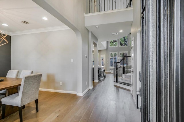 foyer featuring crown molding, arched walkways, baseboards, wood finished floors, and visible vents