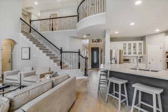living area featuring a toaster, stairs, light wood-type flooring, a towering ceiling, and visible vents