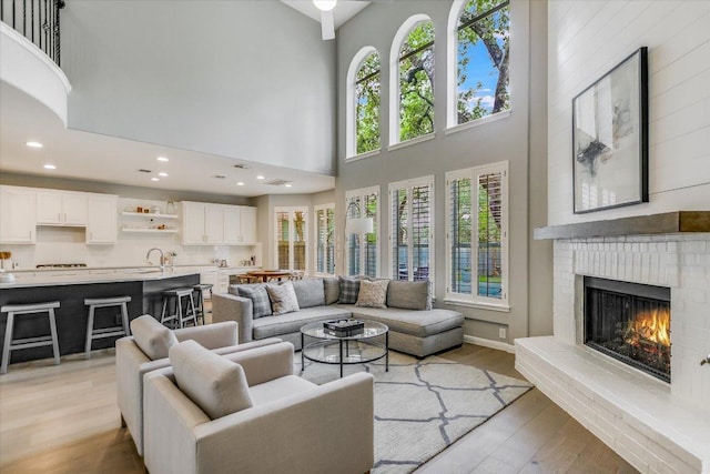 living area with light wood-style floors, recessed lighting, a brick fireplace, and a towering ceiling