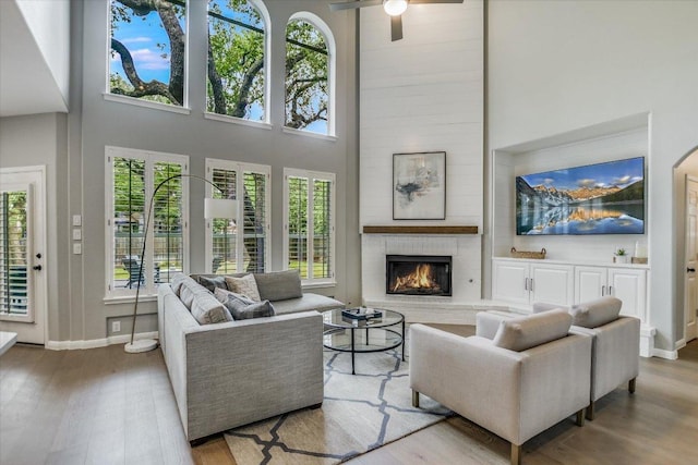 living area featuring a large fireplace, plenty of natural light, wood finished floors, and a high ceiling