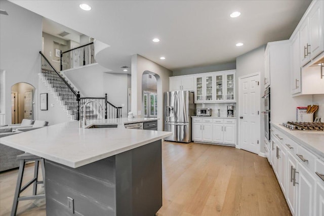 kitchen with white cabinets, appliances with stainless steel finishes, a sink, arched walkways, and a kitchen bar