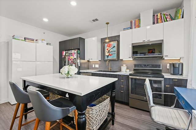 kitchen with a sink, light countertops, stainless steel appliances, wood finished floors, and backsplash