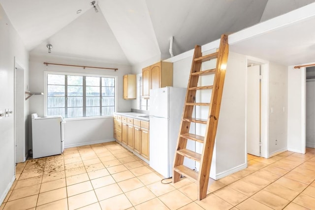 kitchen featuring freestanding refrigerator, lofted ceiling, light brown cabinetry, baseboards, and light countertops