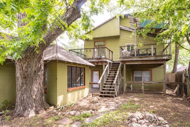 rear view of house featuring a wooden deck, fence, stairway, and concrete block siding