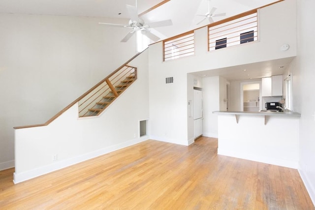 unfurnished living room featuring ceiling fan, visible vents, light wood-style flooring, and stairway