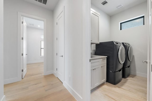 washroom featuring separate washer and dryer, light wood-style flooring, plenty of natural light, and visible vents