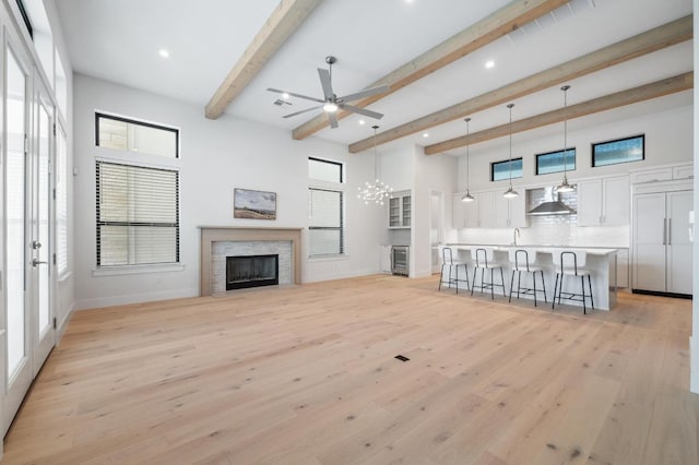 living room with a healthy amount of sunlight, a fireplace, beam ceiling, ceiling fan with notable chandelier, and light wood-style floors