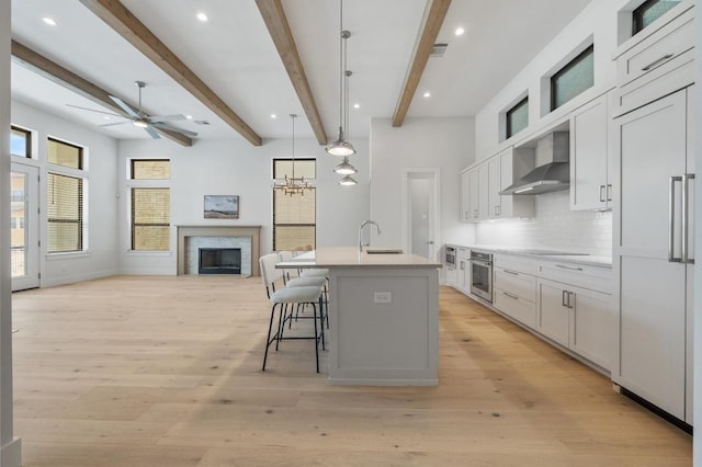 kitchen featuring ceiling fan, a sink, open floor plan, stainless steel oven, and wall chimney exhaust hood