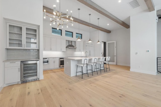 kitchen with decorative backsplash, a kitchen breakfast bar, beamed ceiling, beverage cooler, and wall chimney exhaust hood