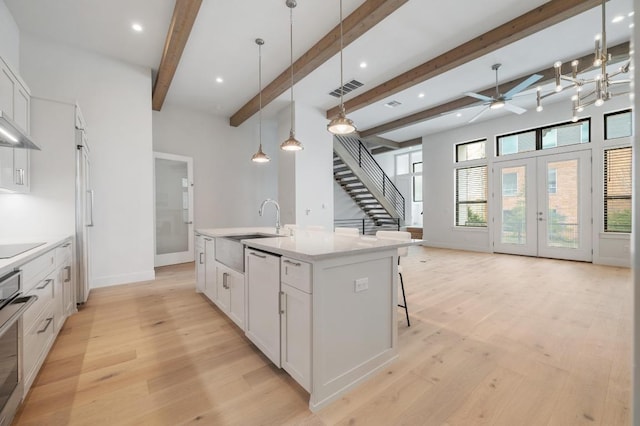 kitchen featuring a ceiling fan, visible vents, a sink, light wood finished floors, and an island with sink