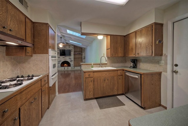 kitchen featuring a sink, brown cabinets, under cabinet range hood, and white appliances