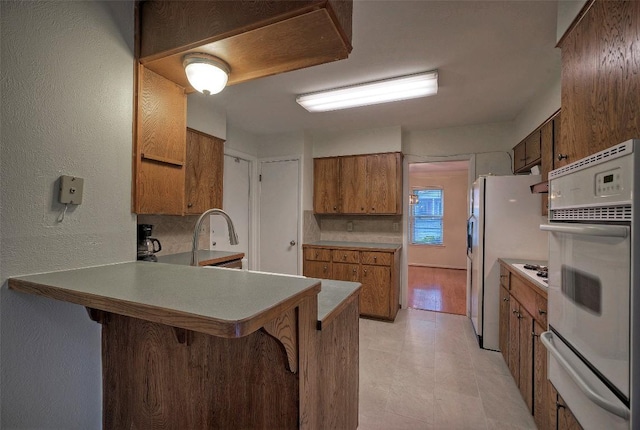kitchen featuring brown cabinets, a breakfast bar, white appliances, a peninsula, and a warming drawer