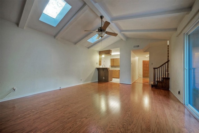 unfurnished living room with beamed ceiling, a skylight, wood finished floors, and stairway