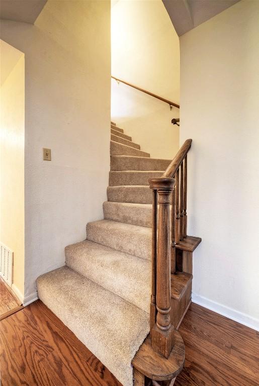 stairway with baseboards, wood finished floors, and visible vents