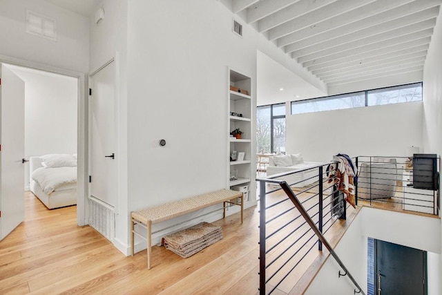hall with beam ceiling, visible vents, wood finished floors, and an upstairs landing
