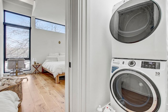 clothes washing area featuring stacked washer and clothes dryer and light wood-style flooring