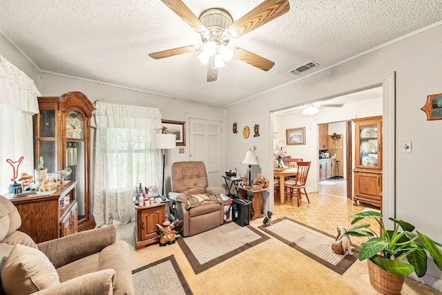 living area with crown molding, a ceiling fan, a textured ceiling, and visible vents