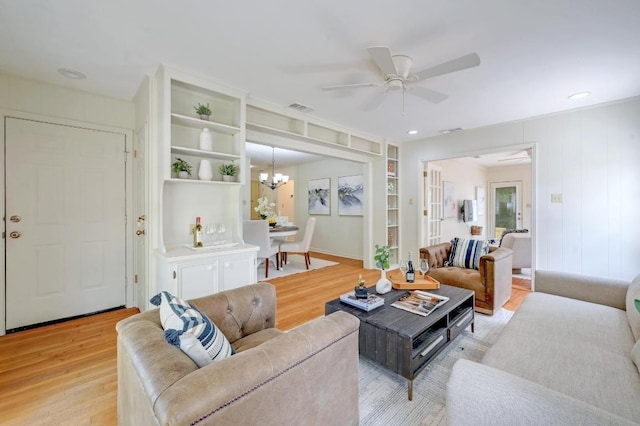 living room featuring light wood-style flooring, a ceiling fan, built in shelves, and a chandelier
