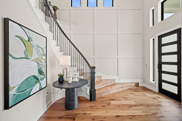 foyer entrance featuring a high ceiling, a decorative wall, stairs, and wood finished floors