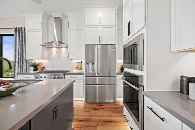 kitchen with appliances with stainless steel finishes, light wood-style flooring, wall chimney exhaust hood, and a wealth of natural light