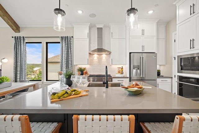 kitchen featuring appliances with stainless steel finishes, a kitchen breakfast bar, wall chimney exhaust hood, decorative light fixtures, and decorative backsplash