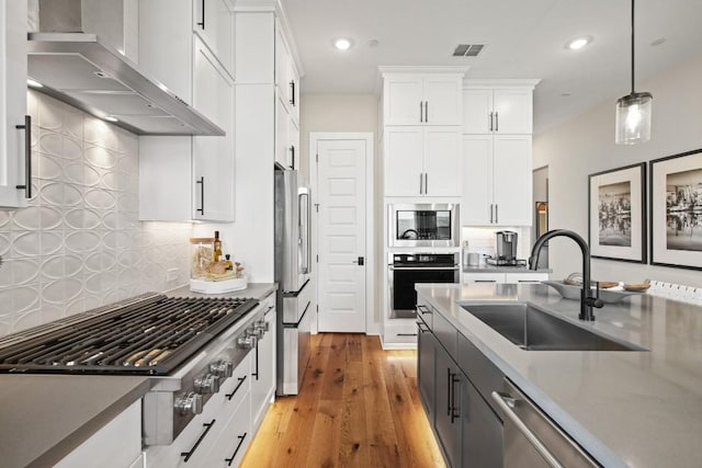 kitchen featuring wall chimney range hood, a sink, white cabinets, stainless steel appliances, and recessed lighting