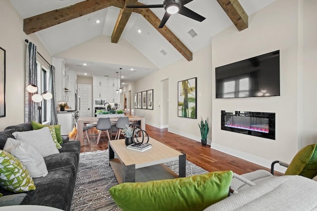 living room with beamed ceiling, a glass covered fireplace, ceiling fan, and dark wood-type flooring