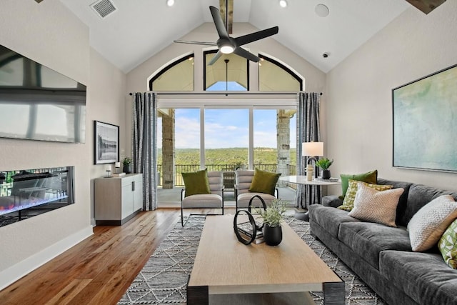 living room with visible vents, a glass covered fireplace, wood finished floors, ceiling fan, and high vaulted ceiling