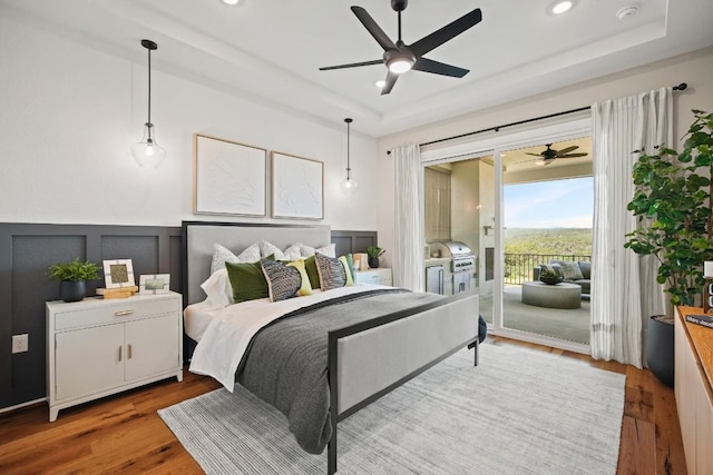 bedroom featuring access to outside, a raised ceiling, and wood finished floors