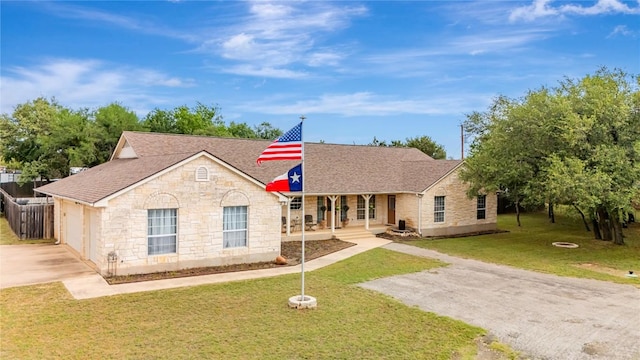view of front of home with covered porch, roof with shingles, a front lawn, concrete driveway, and stone siding