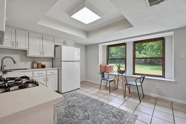 kitchen featuring a sink, freestanding refrigerator, baseboards, a tray ceiling, and visible vents