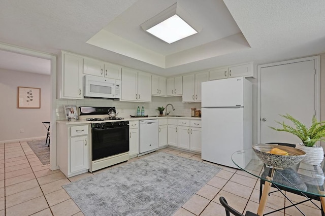 7304 Beckett Rd, Austin, TX 78749 - kitchen featuring white appliances, a tray ceiling, light tile patterned flooring, light countertops, and white cabinets