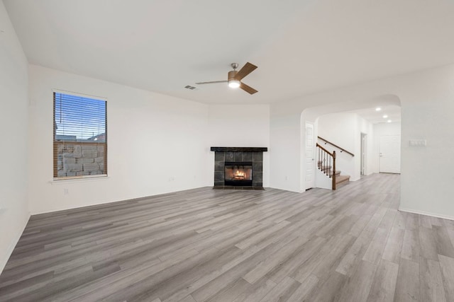 3944 Tufino Ln, Round Rock, TX 78665 - unfurnished living room featuring a tiled fireplace, ceiling fan, wood finished floors, arched walkways, and stairway