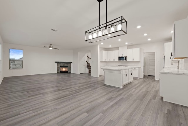 3944 Tufino Ln, Round Rock, TX 78665 - kitchen with stainless steel microwave, a center island, light wood-style floors, a ceiling fan, and white cabinets