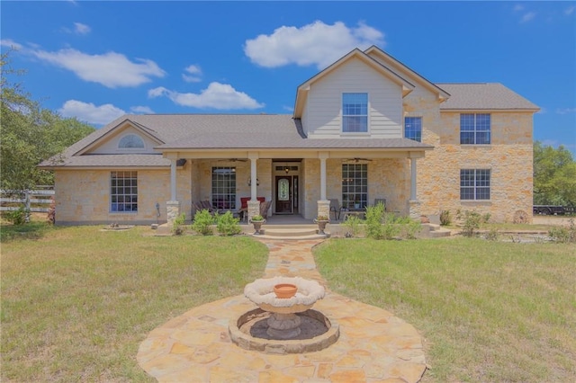 traditional-style house featuring fence, a front yard, a porch, and stone siding